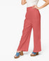 A model wearing high-waisted, wide-leg terracotta pink pants with a textured fabric, styled with a white top and blue platform sandals against a light gray background.