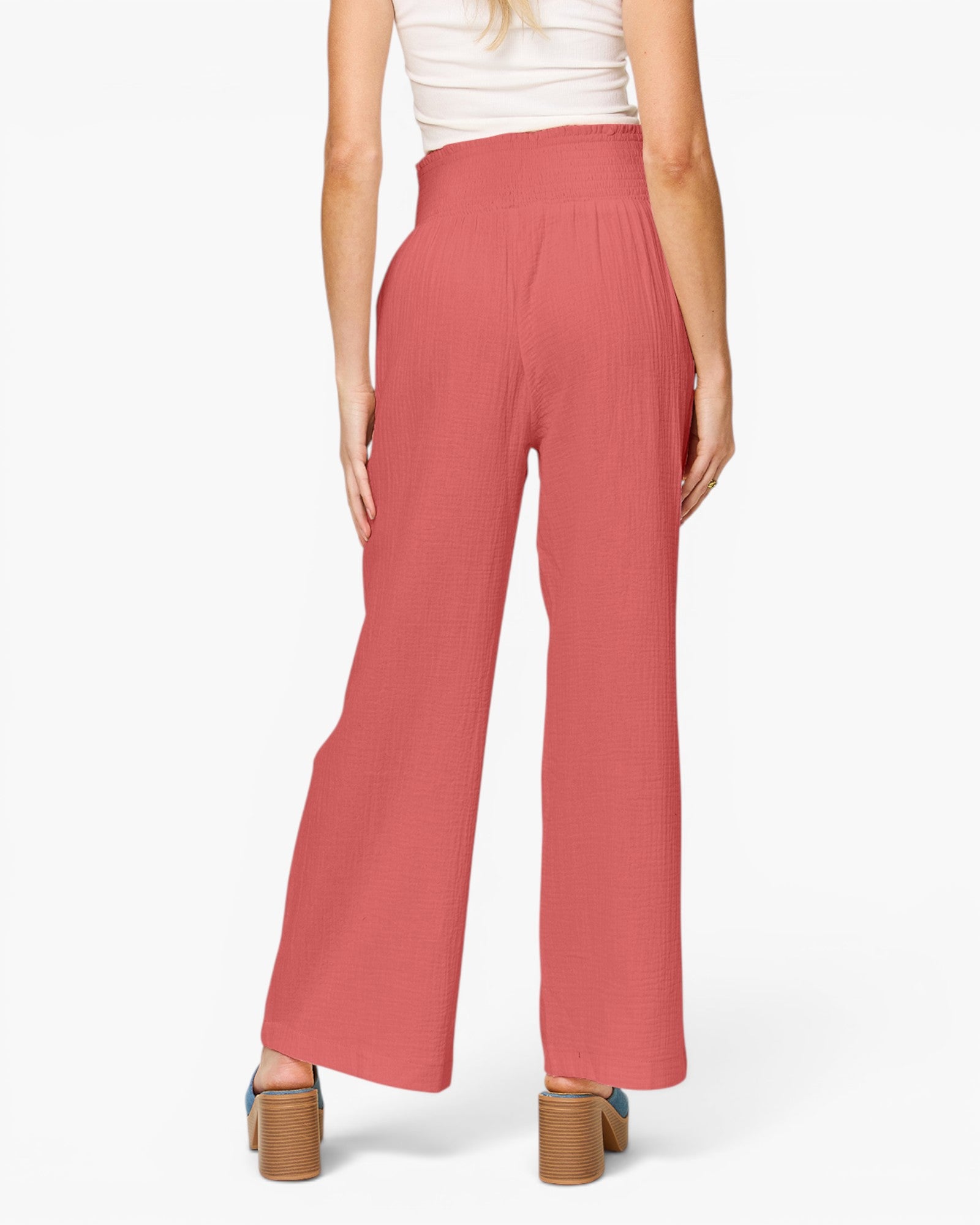 A model shown from the back wearing high-waisted, wide-leg trousers in a dusty rose pink color, paired with a white top and brown block-heel sandals, against a plain white studio background.