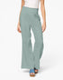 A model from the waist down wearing high-waisted, wide-leg pants in a dusty sage green color, paired with a white top and blue platform sandals, against a plain white studio background.
