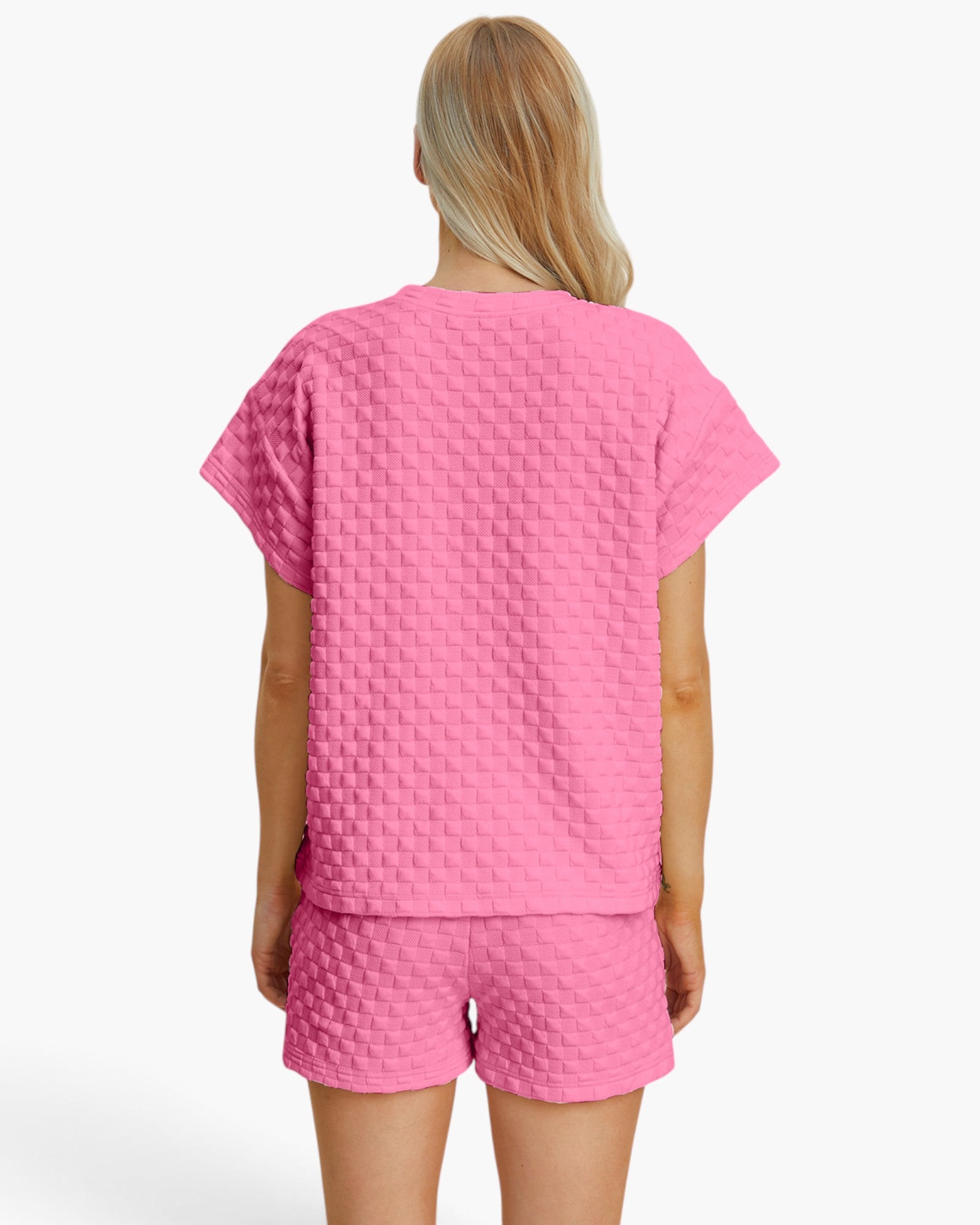 A woman shown from the back wearing a bright pink short-sleeve top and matching shorts with a textured waffle pattern, against a plain white studio background.