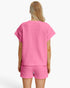 A woman shown from the back wearing a bright pink short-sleeve top and matching shorts with a textured waffle pattern, against a plain white studio background.