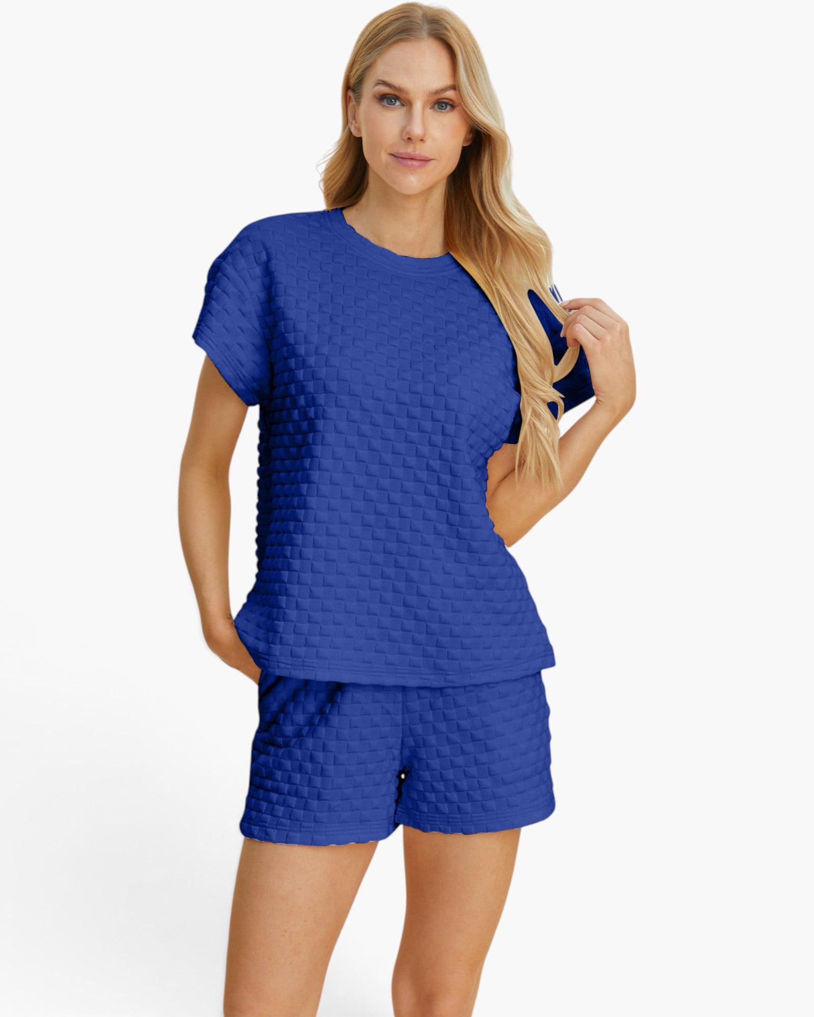 A woman modeling a matching royal blue two-piece lounge set with a short-sleeve top and shorts, both featuring a textured, quilted block pattern, against a plain white studio background.