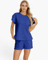 A woman modeling a matching royal blue two-piece lounge set with a short-sleeve top and shorts, both featuring a textured, quilted block pattern, against a plain white studio background.