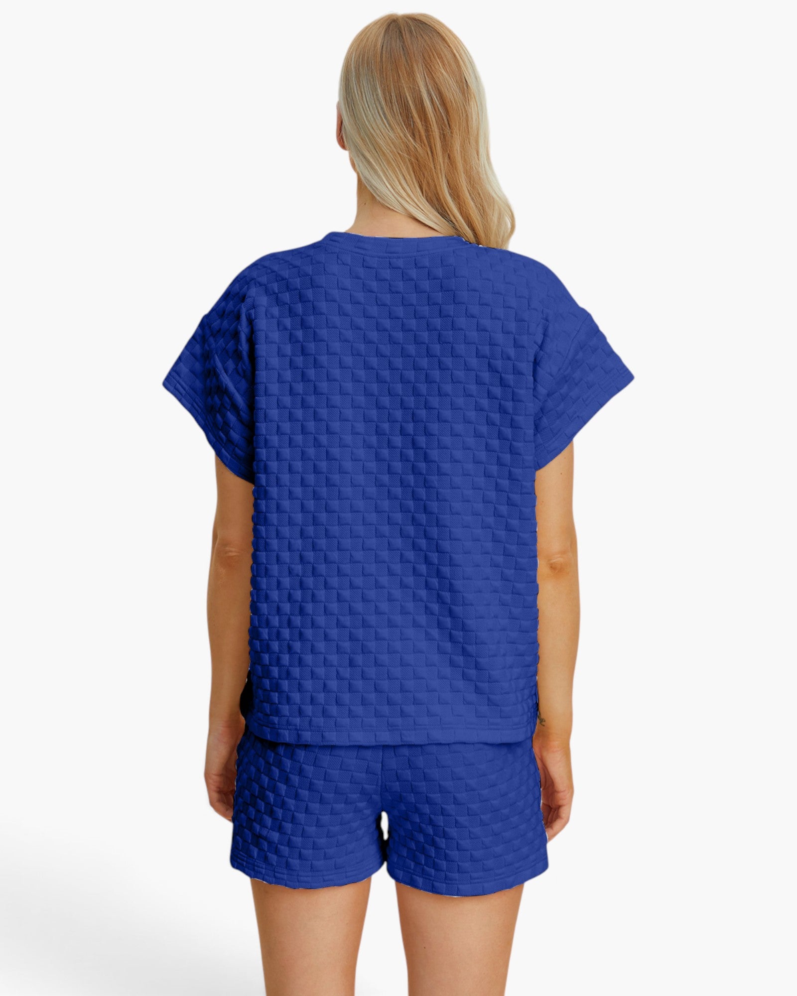 A woman shown from the back wearing a royal blue short-sleeve top and matching shorts with a textured, quilted checkerboard pattern, set against a plain white studio background.