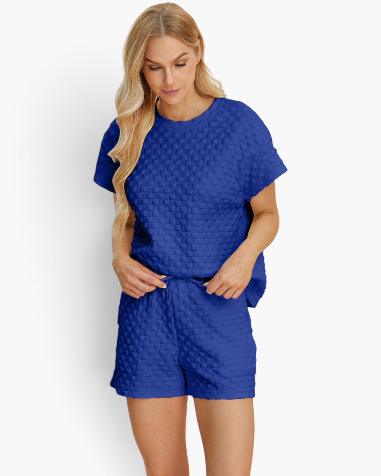 A woman modeling a matching royal blue two-piece lounge set with a textured, quilted pattern. The set includes a short-sleeve top and coordinating shorts, shown against a plain white studio background.
