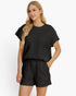 A woman modeling a matching black short-sleeve top and shorts set with a textured, quilted pattern against a plain white background.