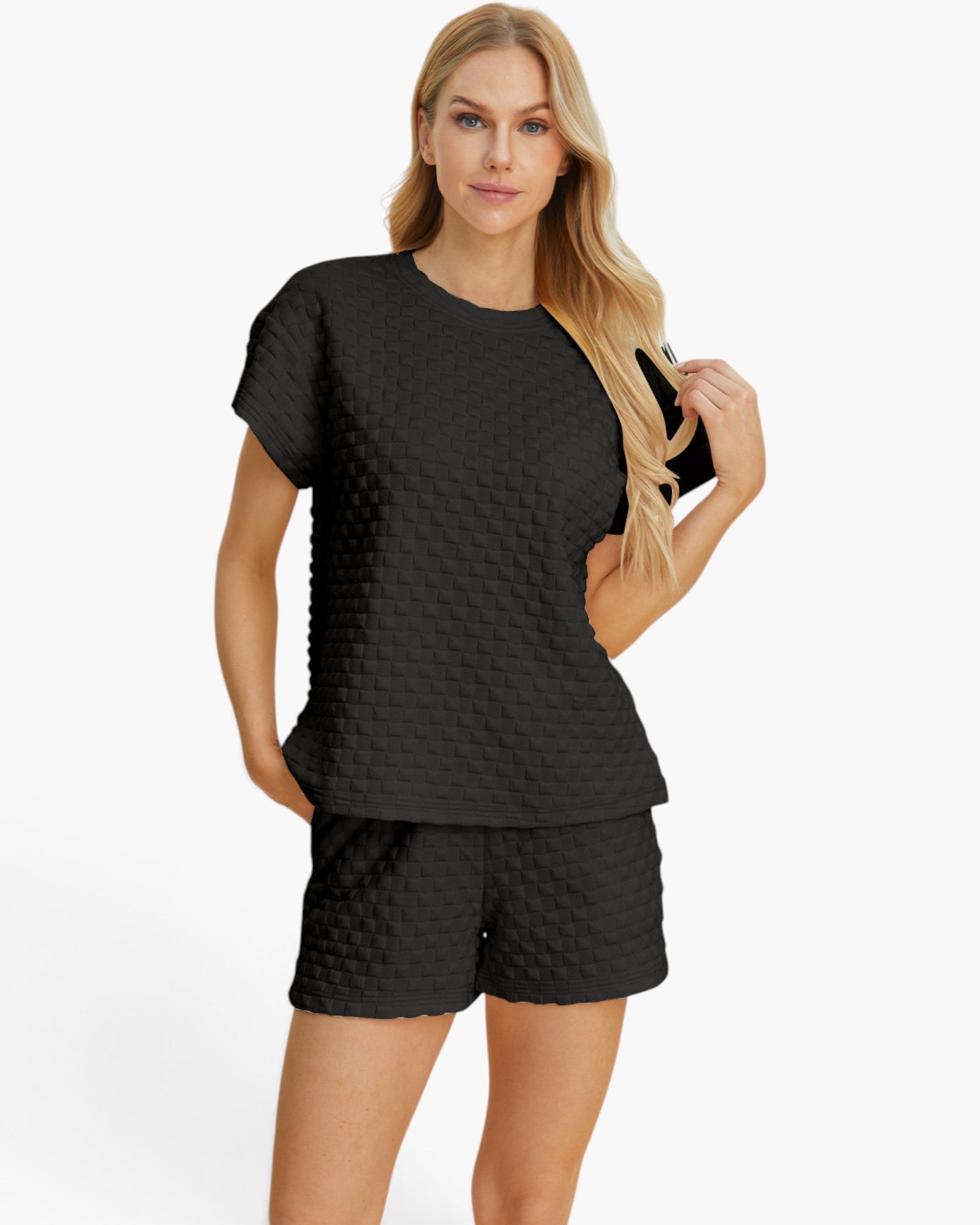 A woman modeling a black two-piece lounge set featuring a short-sleeve top and matching shorts, both with a textured, quilted waffle pattern, against a plain white studio background.