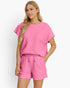 A woman modeling a bright pink two-piece set featuring a short-sleeve top and matching shorts, both with a textured waffle-weave pattern, against a plain white background.