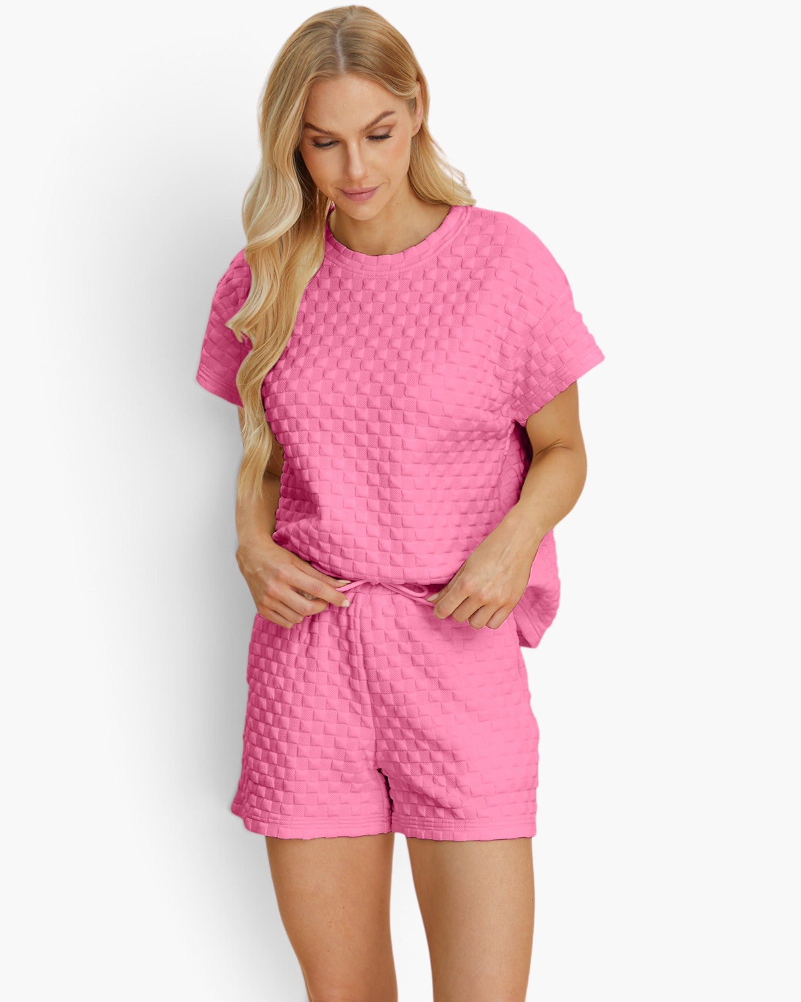 A woman modeling a bright pink two-piece lounge set featuring a short-sleeve top and matching shorts, both with a textured waffle-knit pattern, against a clean white background.
