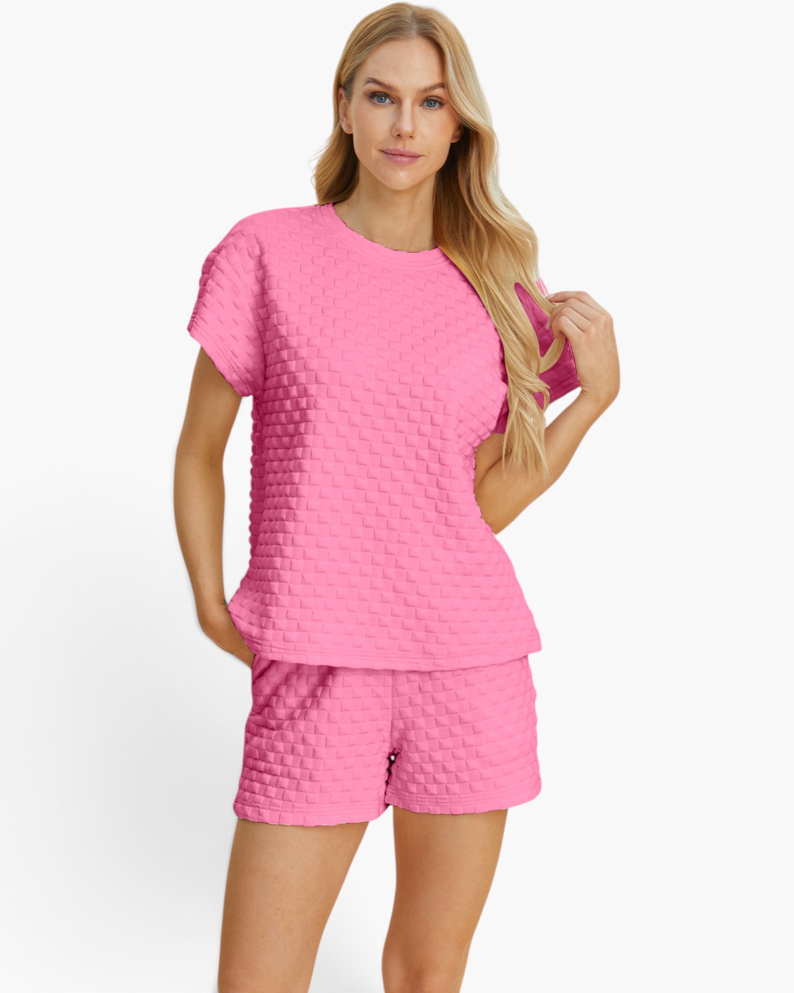 A woman modeling a bright pink two-piece lounge set featuring a short-sleeve top and matching shorts, both with a textured waffle-grid pattern, against a plain white studio background.