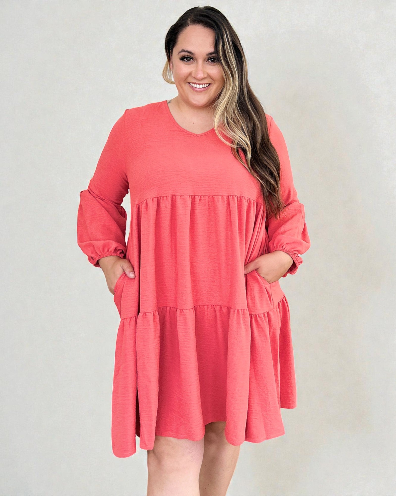 Woman wearing a coral dress with long sleeves against a plain background