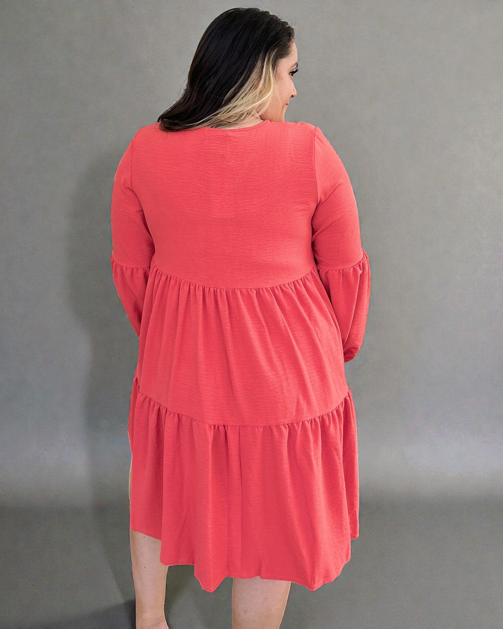 Woman wearing a coral dress against a gray background