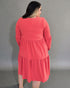 Woman wearing a coral dress against a gray background