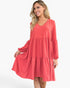 A woman modeling a tiered long-sleeve dress in a coral pink color, shown against a plain white studio background.