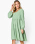 A woman modeling a light sage green tiered dress with long balloon sleeves and a V-neckline, set against a plain white studio background.