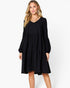 A woman modeling a black long-sleeve tiered dress with a V-neckline, photographed against a clean white studio background.