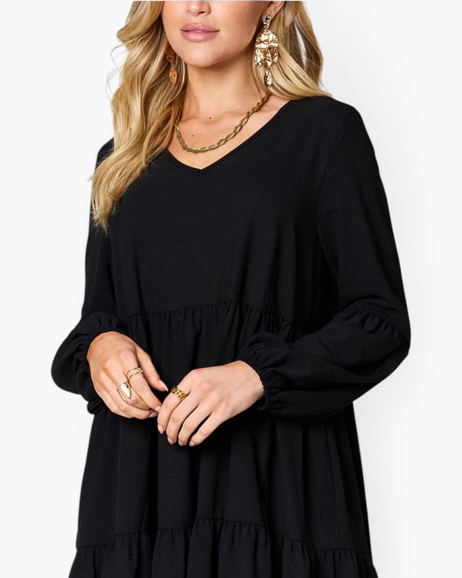 A woman wearing a black long-sleeve tiered dress with a V-neckline, shown from the shoulders to the hips against a plain light background.