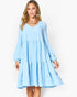 A woman modeling a light blue tiered long-sleeve dress with a V-neckline, photographed against a plain white studio background.