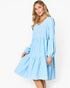 A woman modeling a light blue tiered long-sleeve dress with a V-neckline, photographed against a clean white studio background.