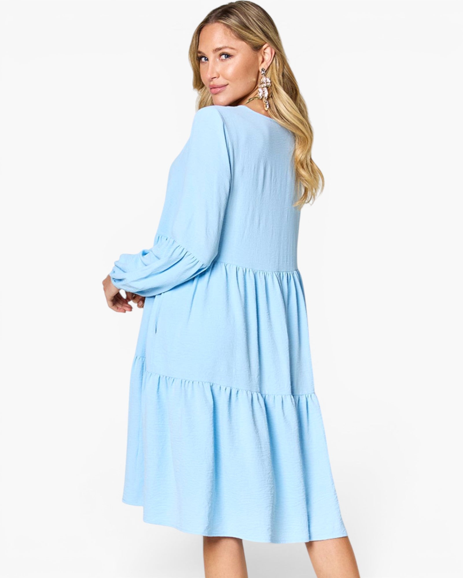 A woman modeling a light blue tiered dress with long sleeves, shown from the back against a plain white studio background.