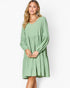 A woman modeling a sage green tiered long-sleeve dress with a V-neckline, photographed against a plain white studio background.