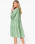 A woman modeling a sage green tiered midi dress with three-quarter sleeves, shown from a three-quarter back angle against a plain white studio background.