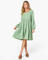 A woman modeling a sage green tiered long-sleeve dress with a V-neckline, paired with brown heeled sandals against a plain white studio background.