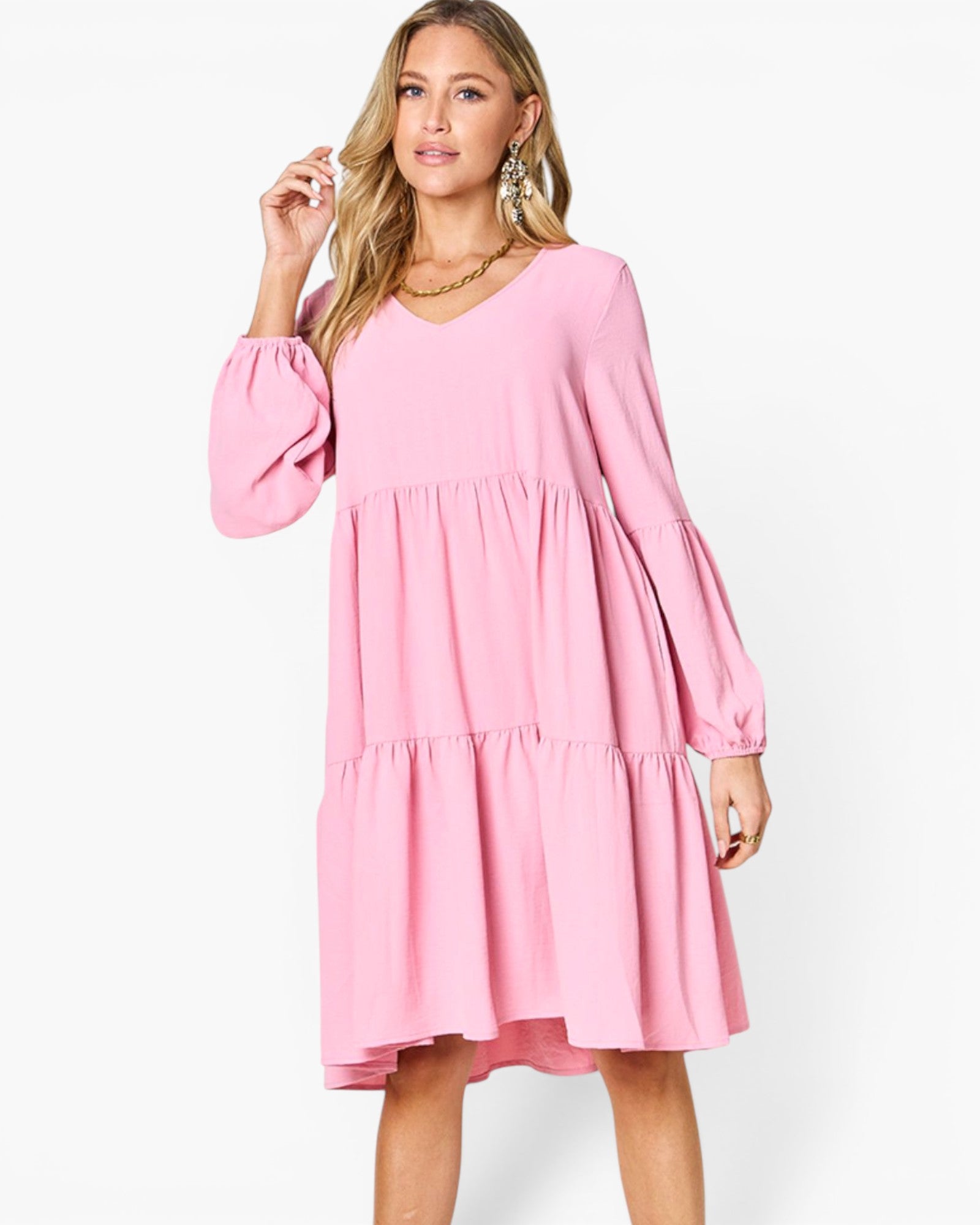 A woman modeling a pink tiered long-sleeve dress with a V-neckline, photographed against a clean white studio background.