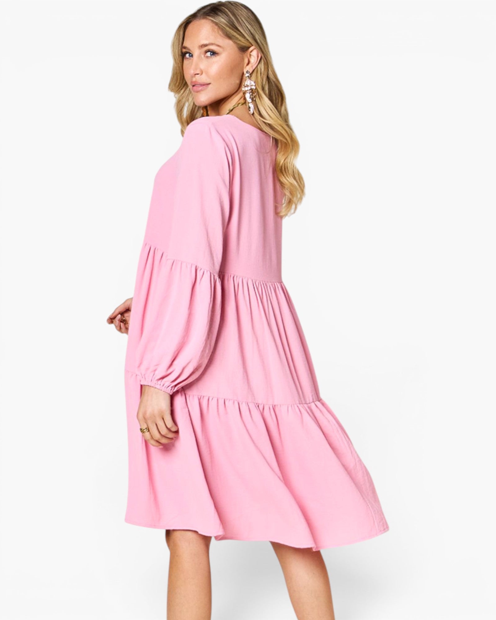 A woman modeling a pink tiered long-sleeve dress from the back, shown against a plain white studio background.