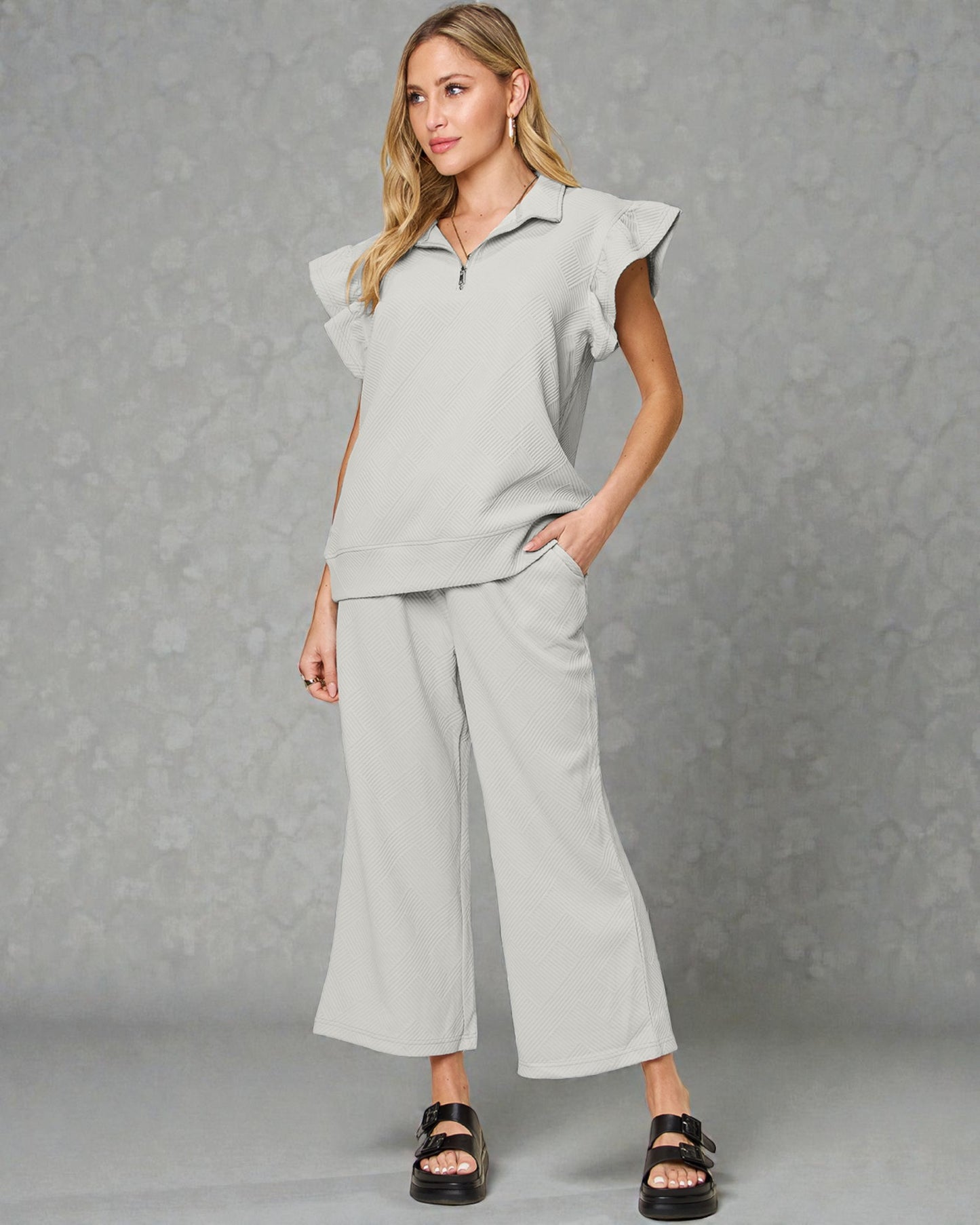 Woman wearing a light gray outfit with ruffled sleeves against a gray background