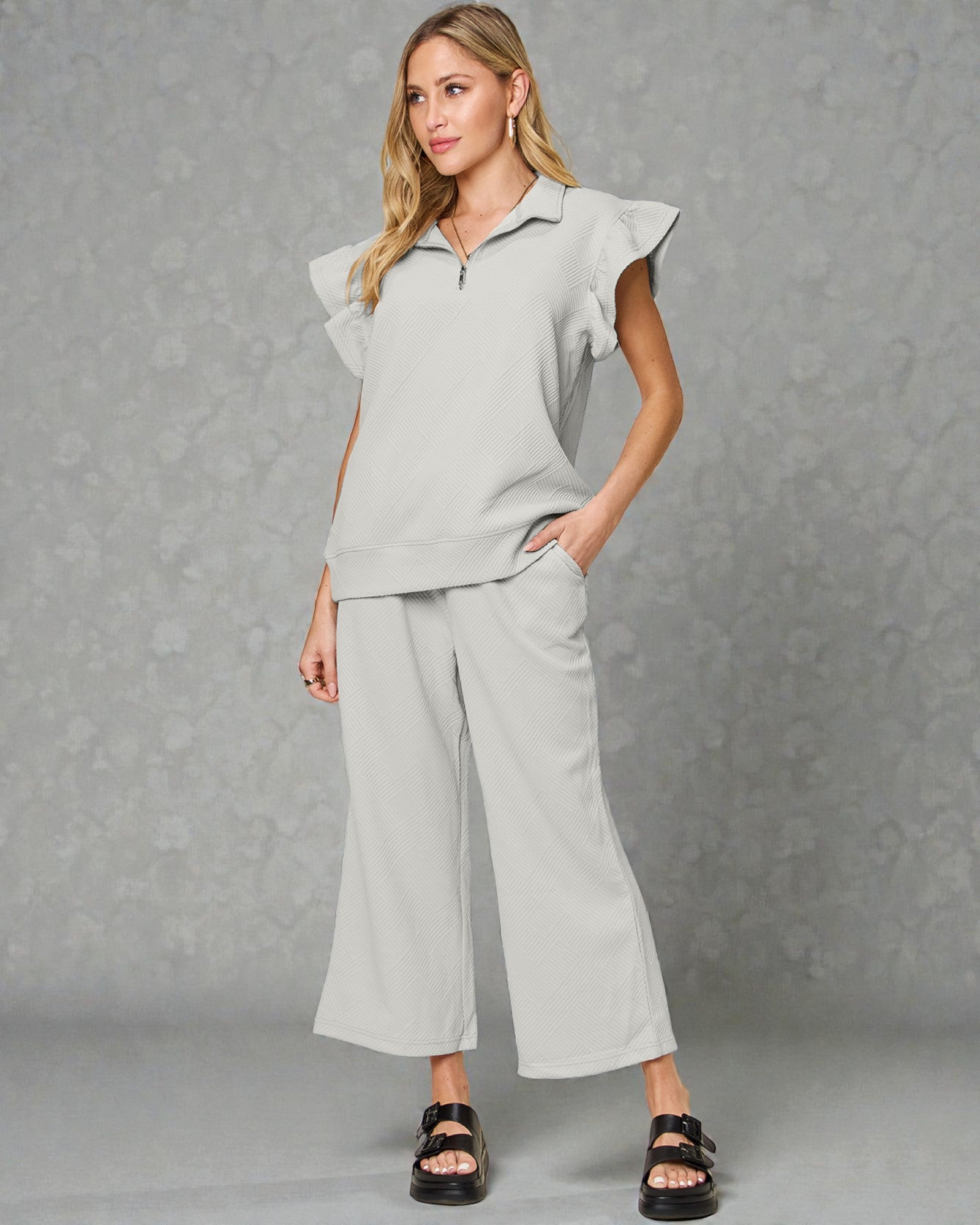 Woman wearing a light gray outfit with ruffled sleeves against a gray background