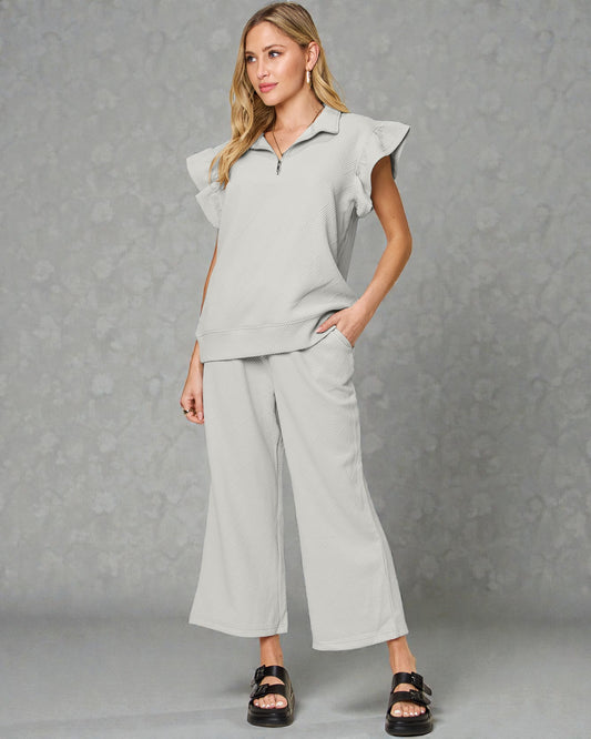 Woman wearing a light gray outfit with ruffled sleeves against a gray background