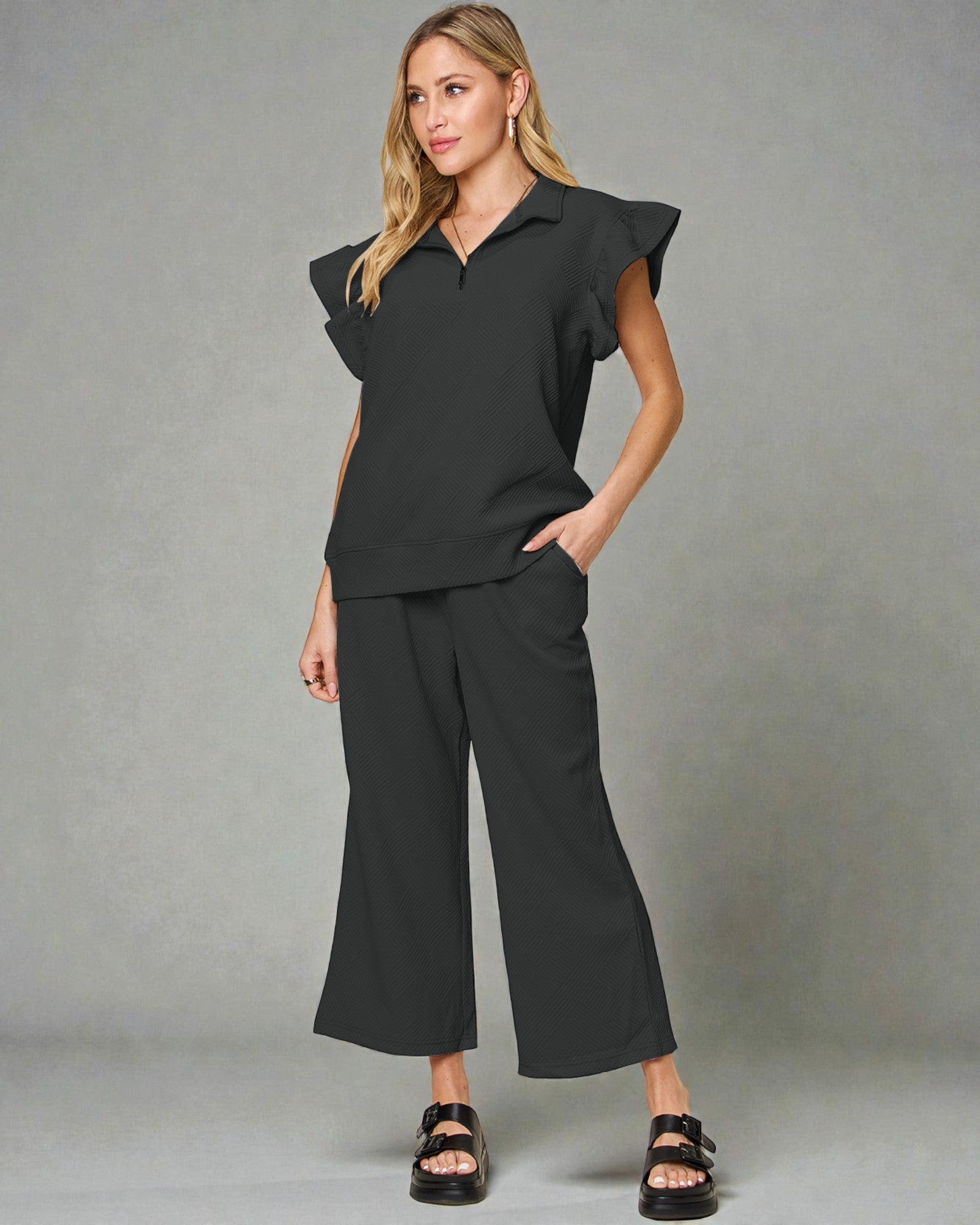 Woman wearing a black outfit with ruffled sleeves against a gray background