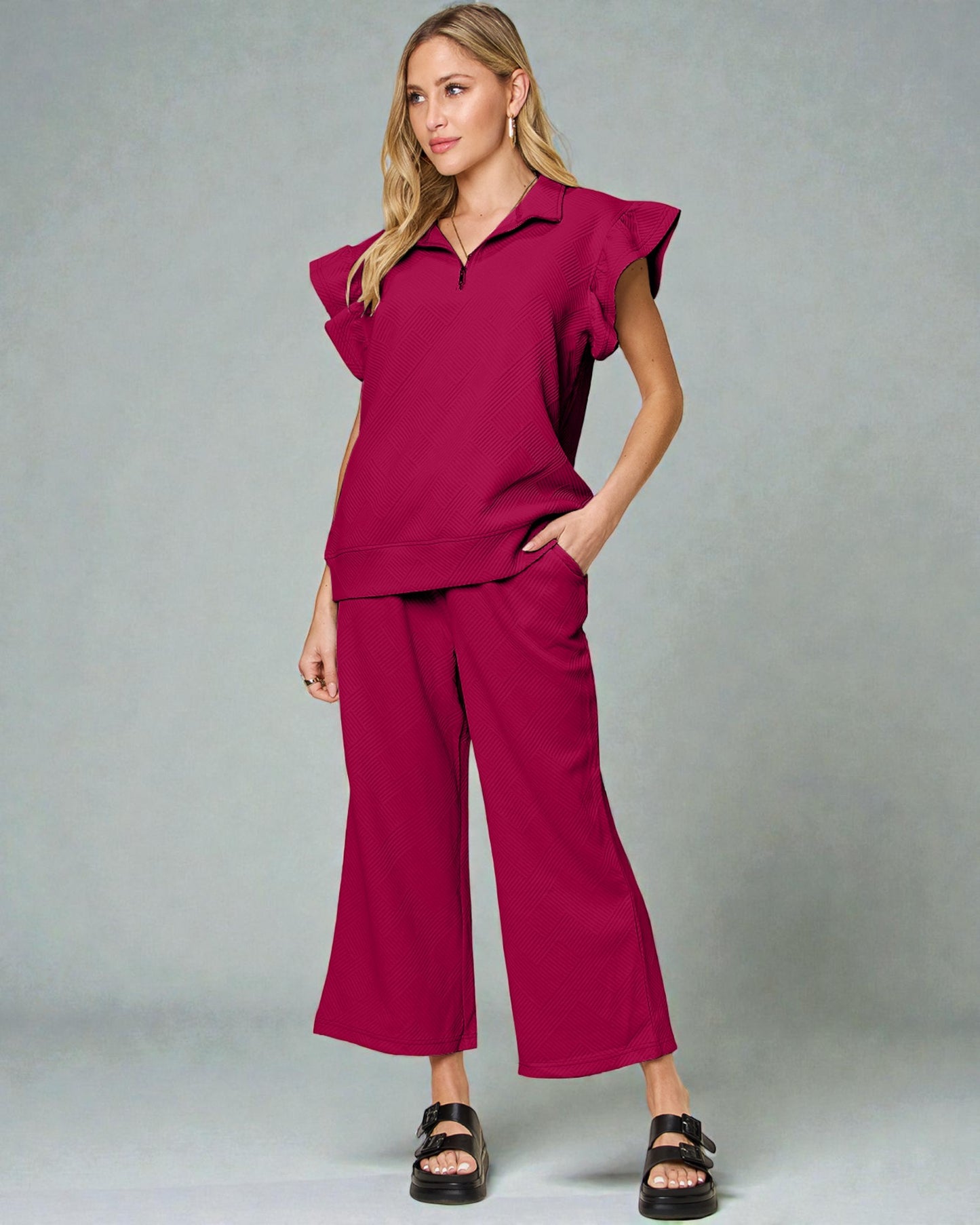 Woman wearing a magenta outfit with ruffled sleeves against a gray background