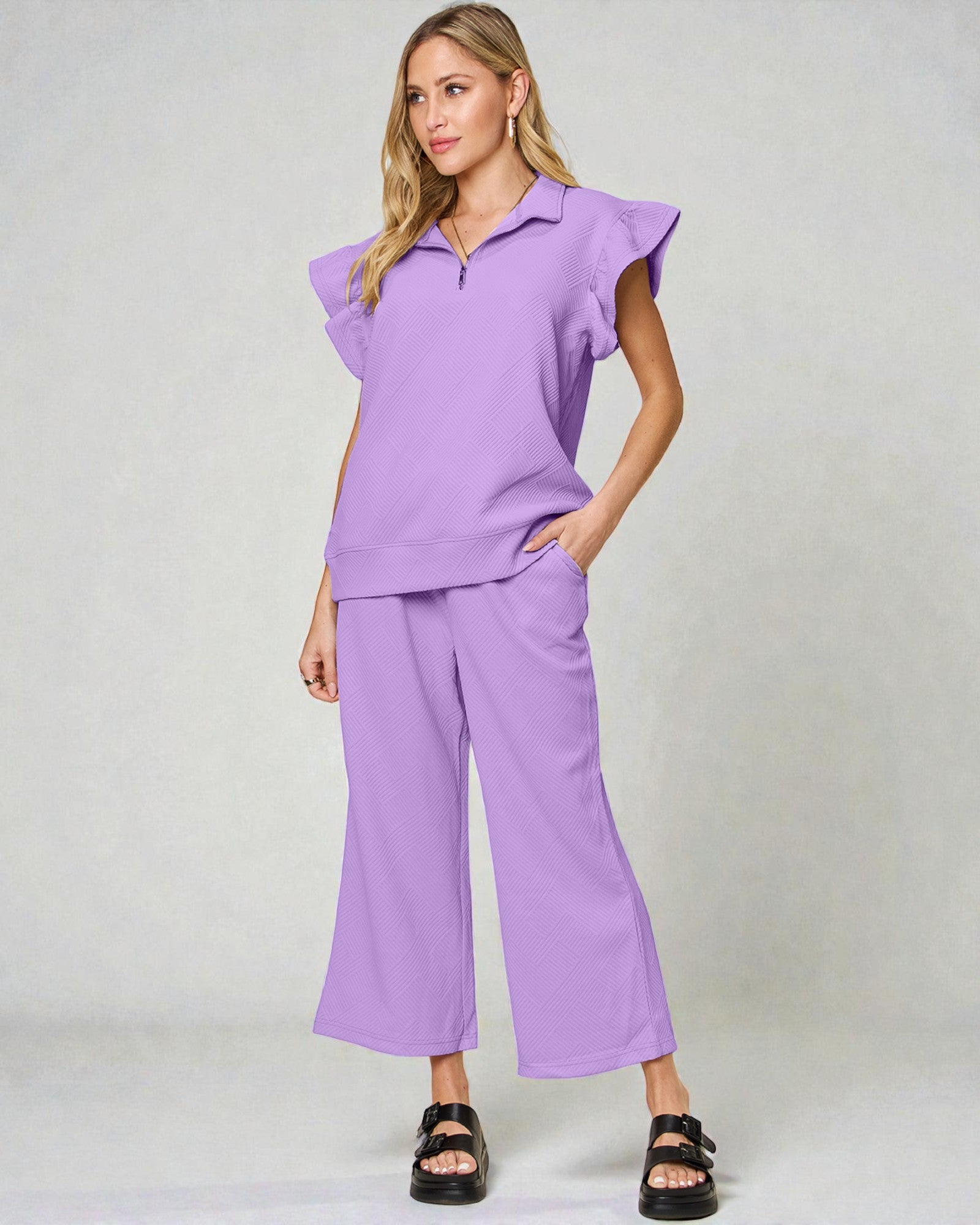 Woman wearing a purple outfit with ruffled sleeves on a white background