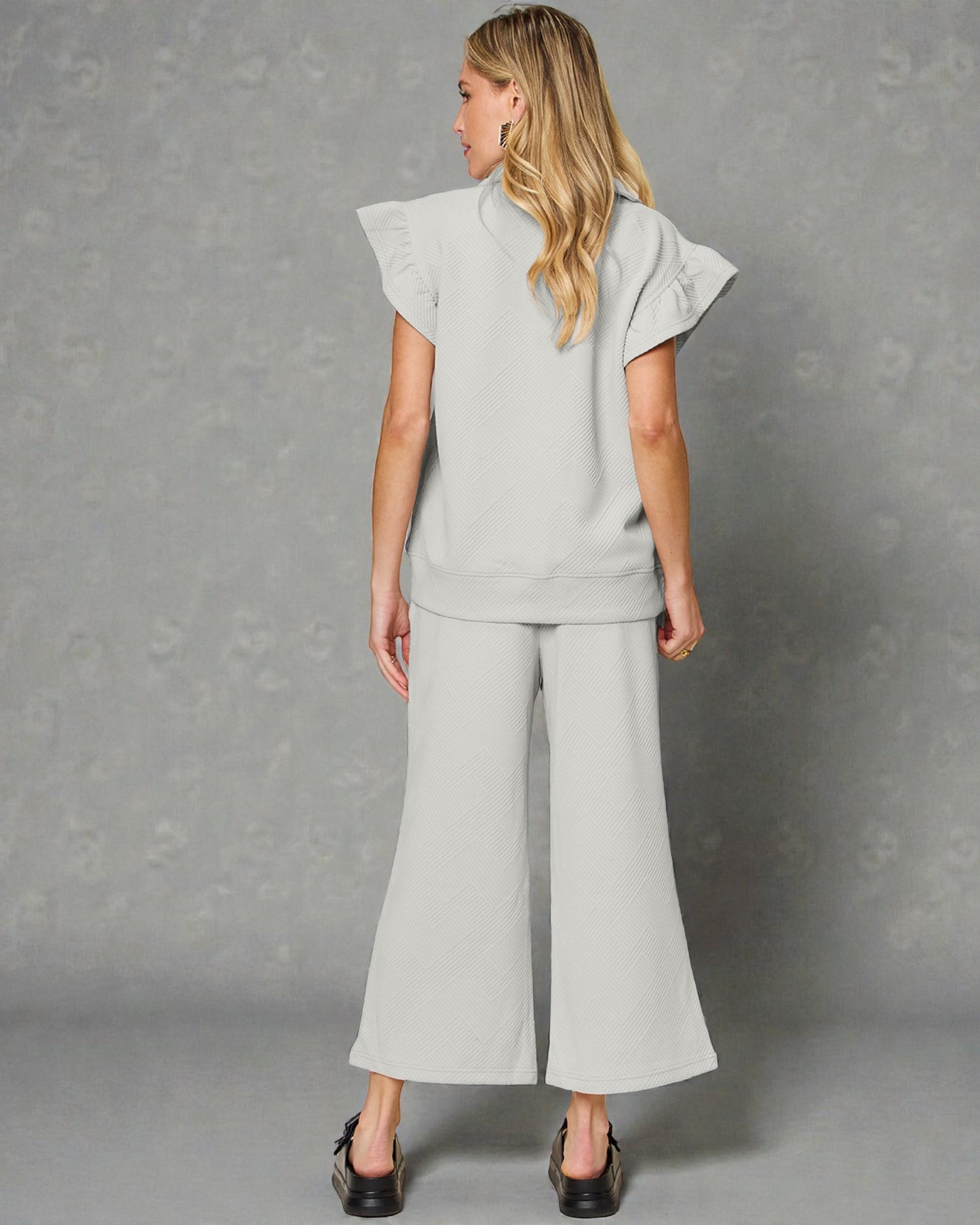 Woman wearing a light gray outfit with wide-leg pants against a gray background