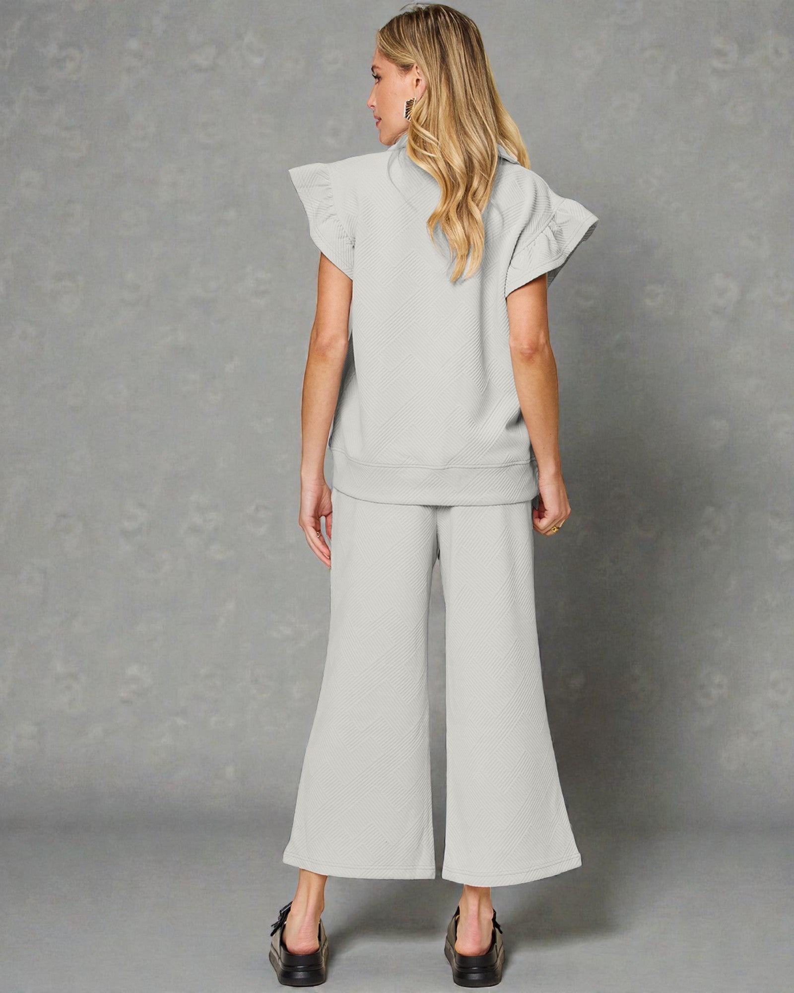 Woman wearing a light gray outfit with wide-leg pants against a gray background