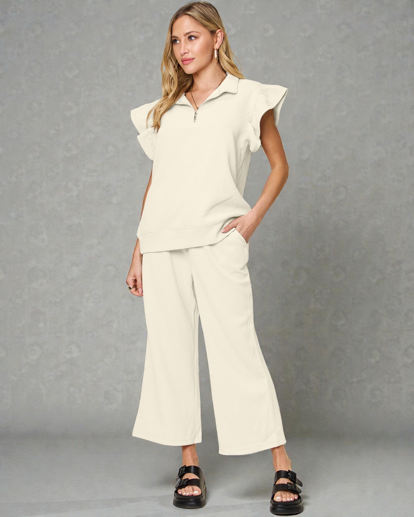 Woman wearing a cream-colored outfit with a top and wide-leg pants on a gray background
