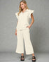 Woman wearing a cream-colored outfit with a top and wide-leg pants on a gray background