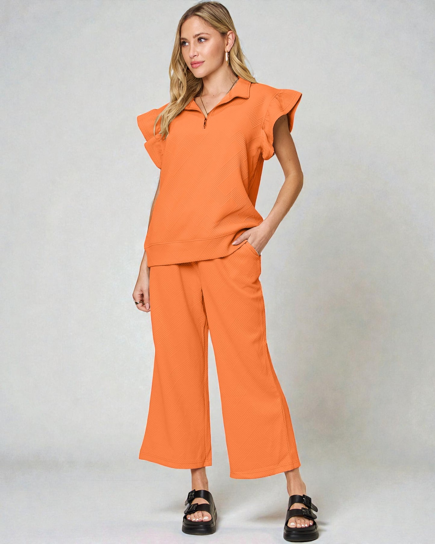 Woman wearing an orange outfit with ruffled top and wide-leg pants on a plain background