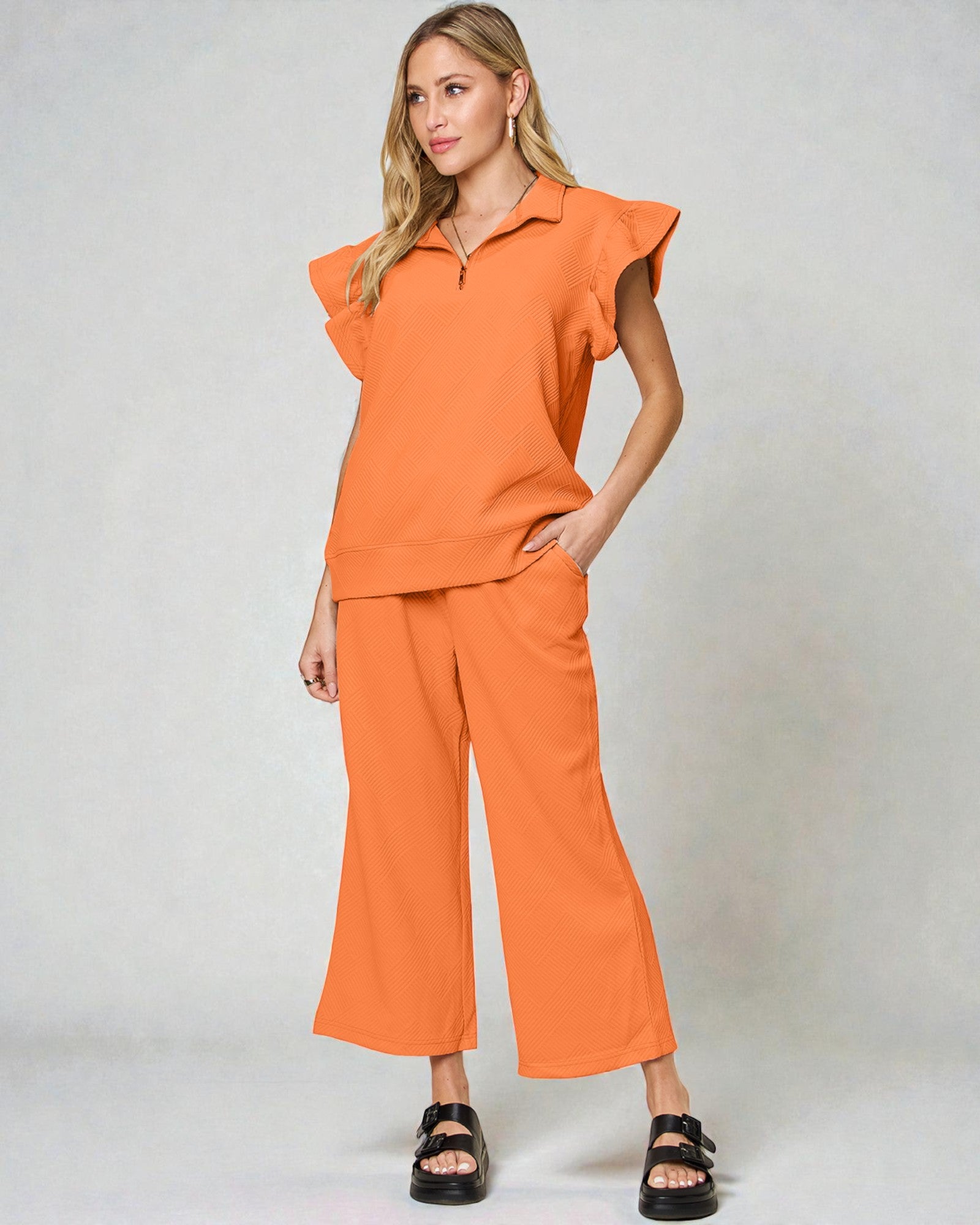 Woman wearing an orange outfit with ruffled top and wide-leg pants on a plain background
