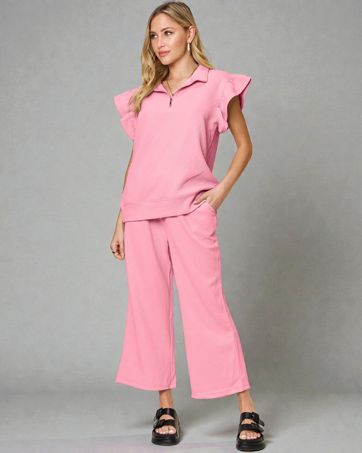 Woman wearing a pink outfit with ruffled sleeves against a gray background