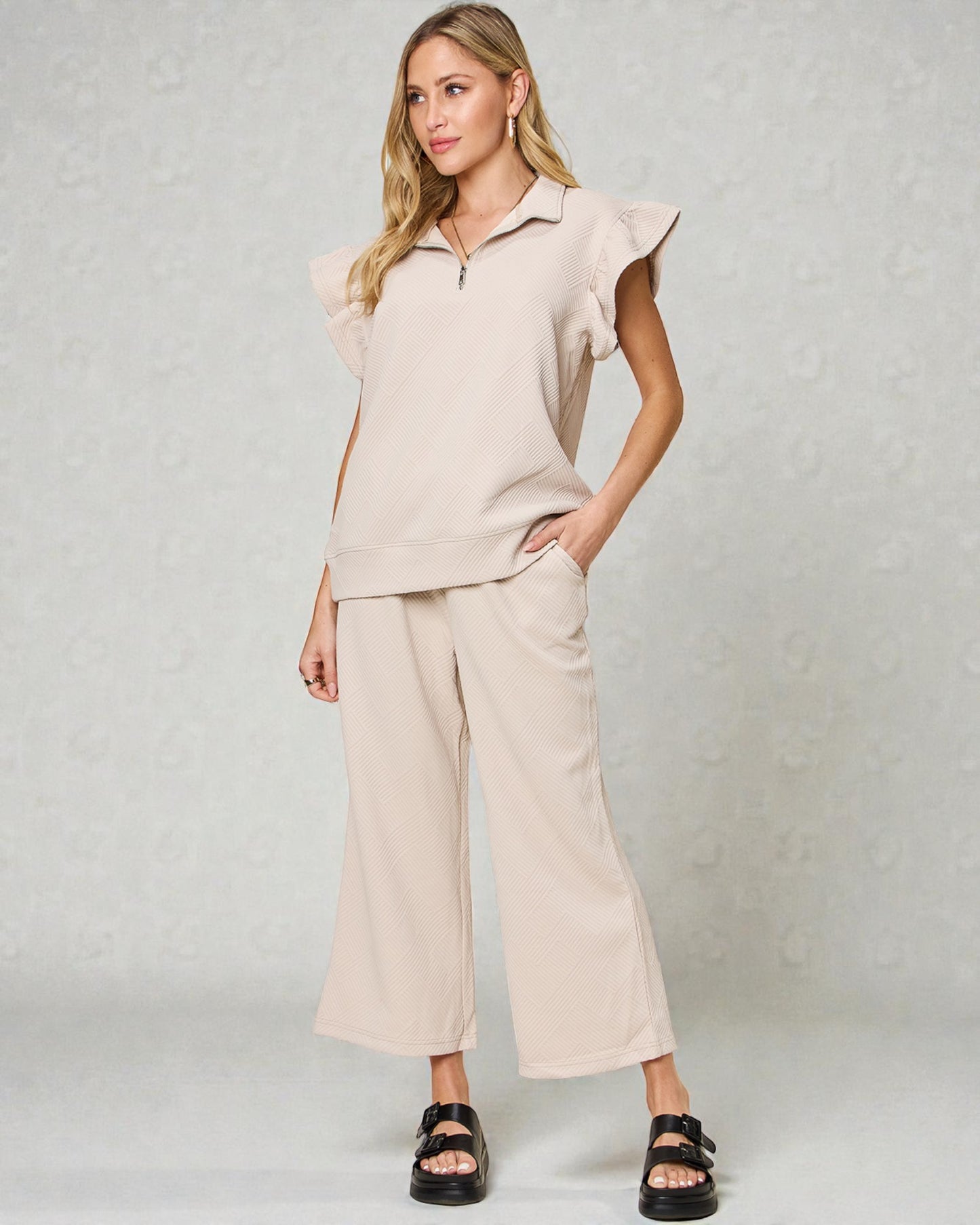 Woman wearing a beige outfit with ruffled sleeves against a plain background