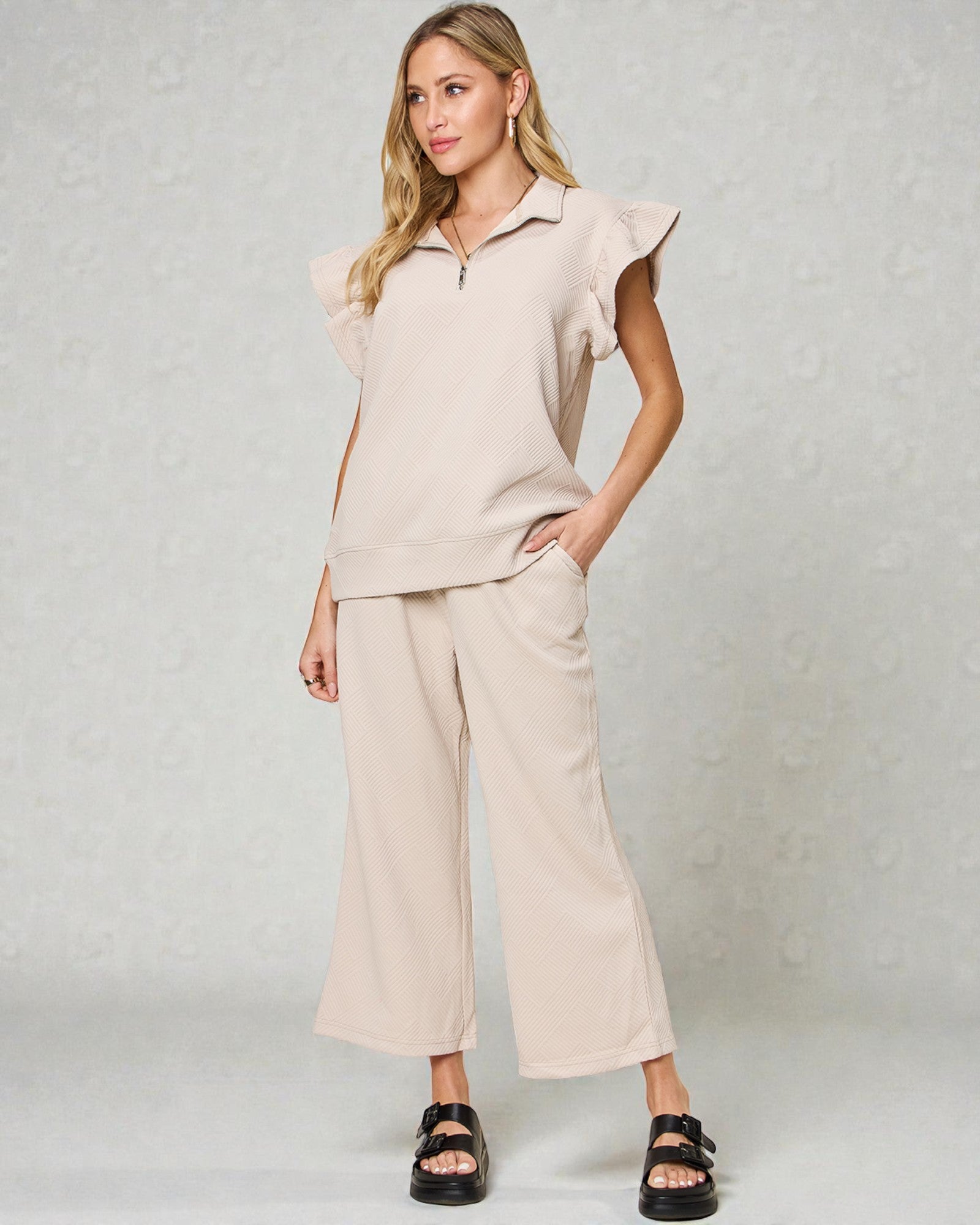 Woman wearing a beige outfit with ruffled sleeves against a plain background