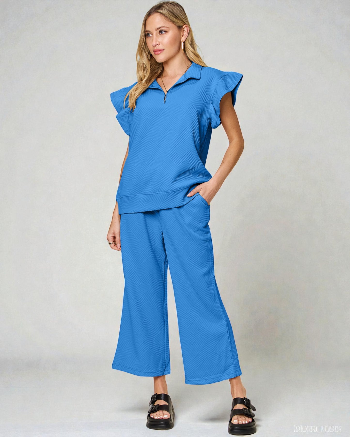 Woman wearing a blue outfit with ruffled sleeves on a gray background