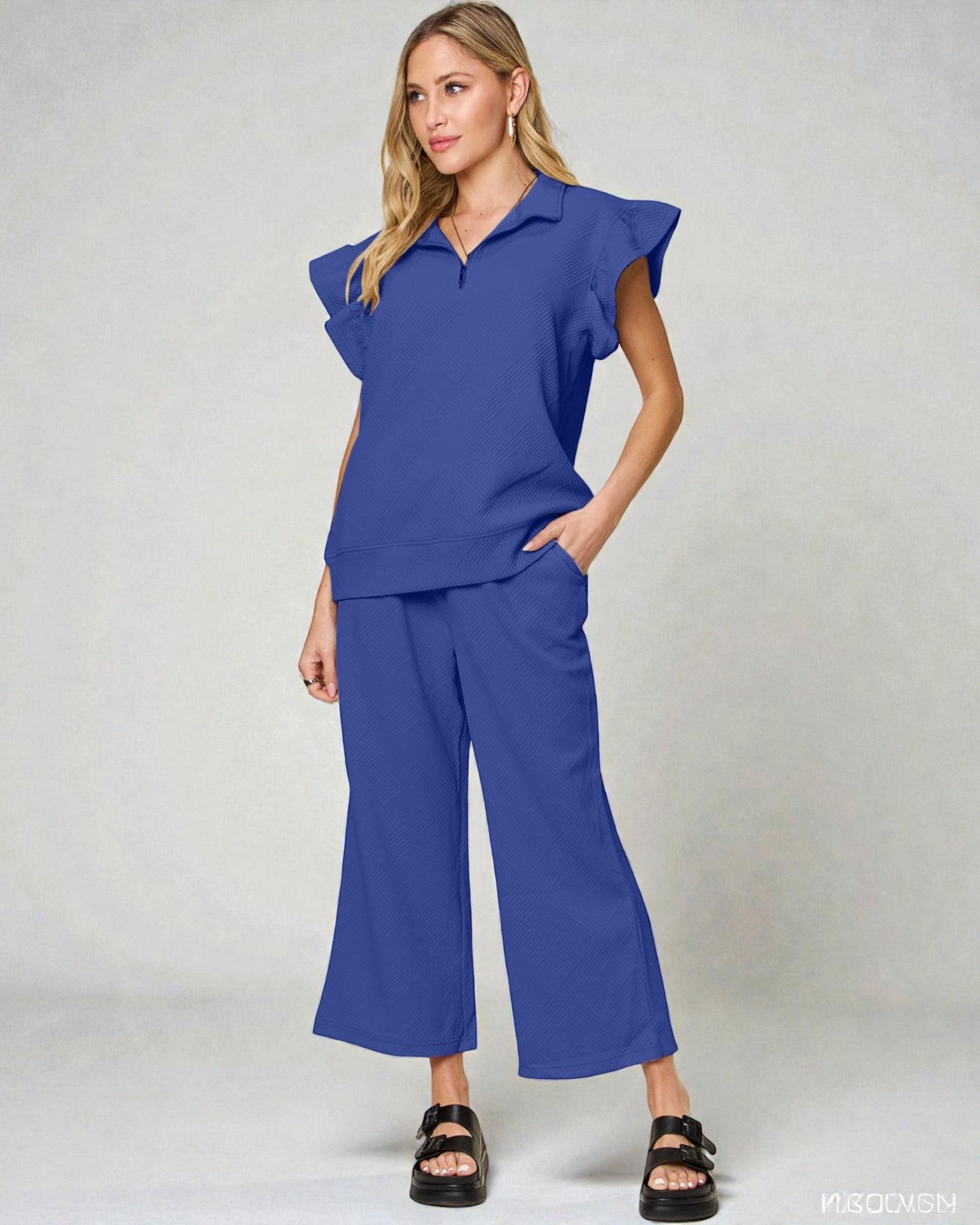 Woman wearing a blue outfit with ruffled sleeves on a plain background