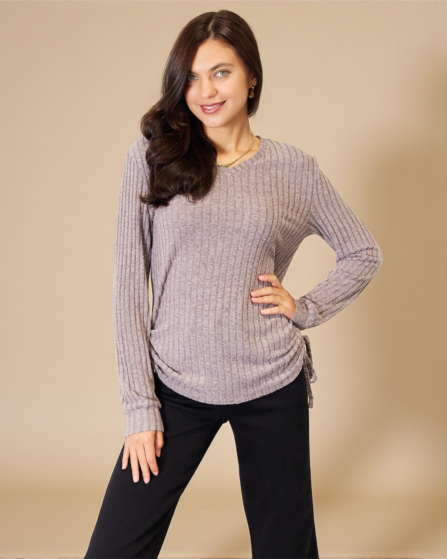Woman wearing a gray ribbed sweater and black pants against a beige background