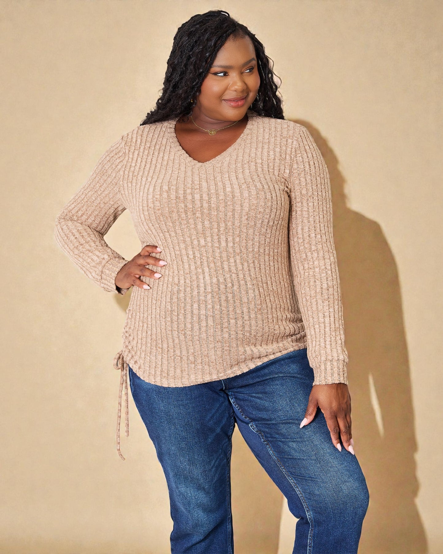Woman wearing a beige sweater and blue jeans against a beige background