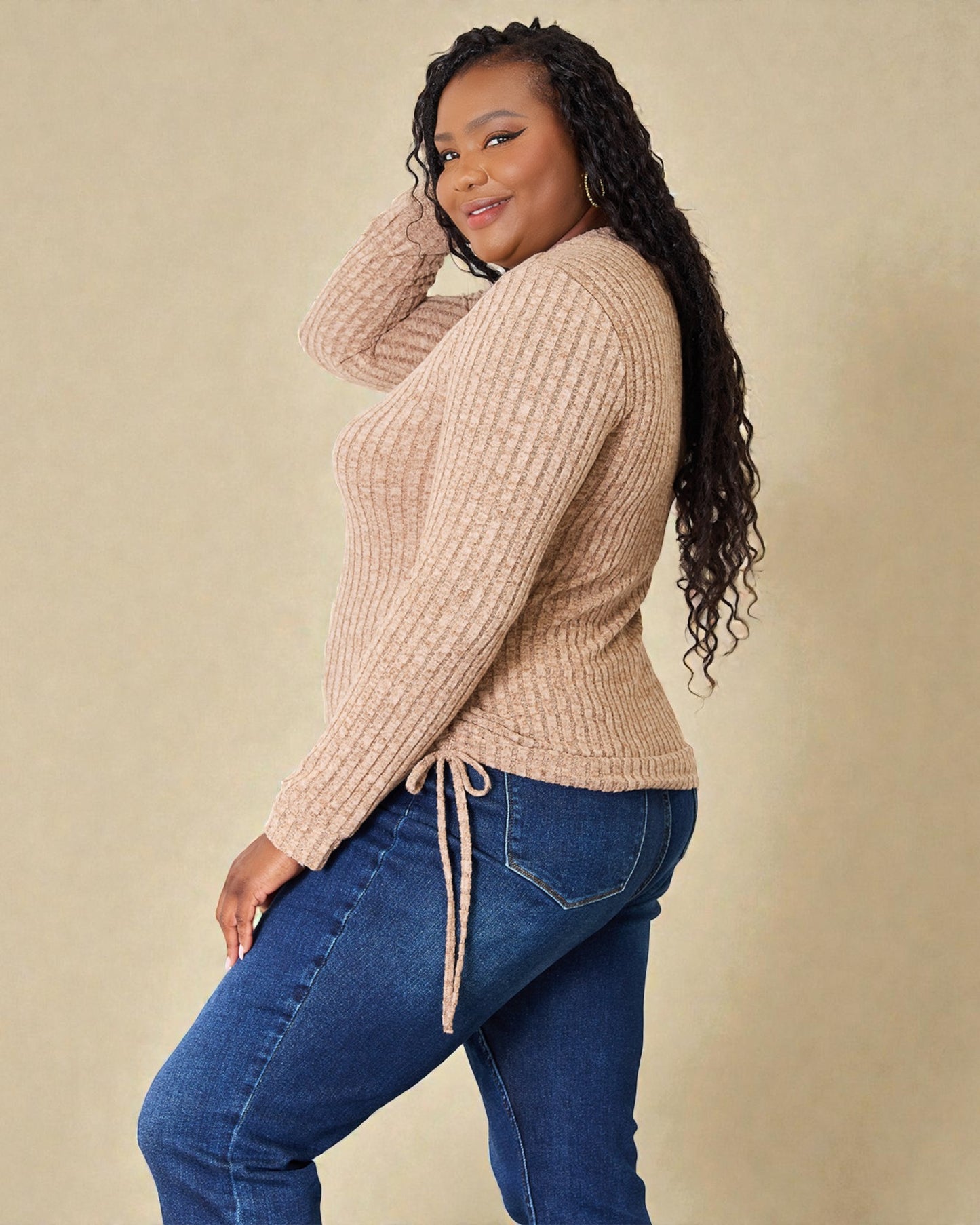 Woman wearing a beige sweater and blue jeans against a beige background