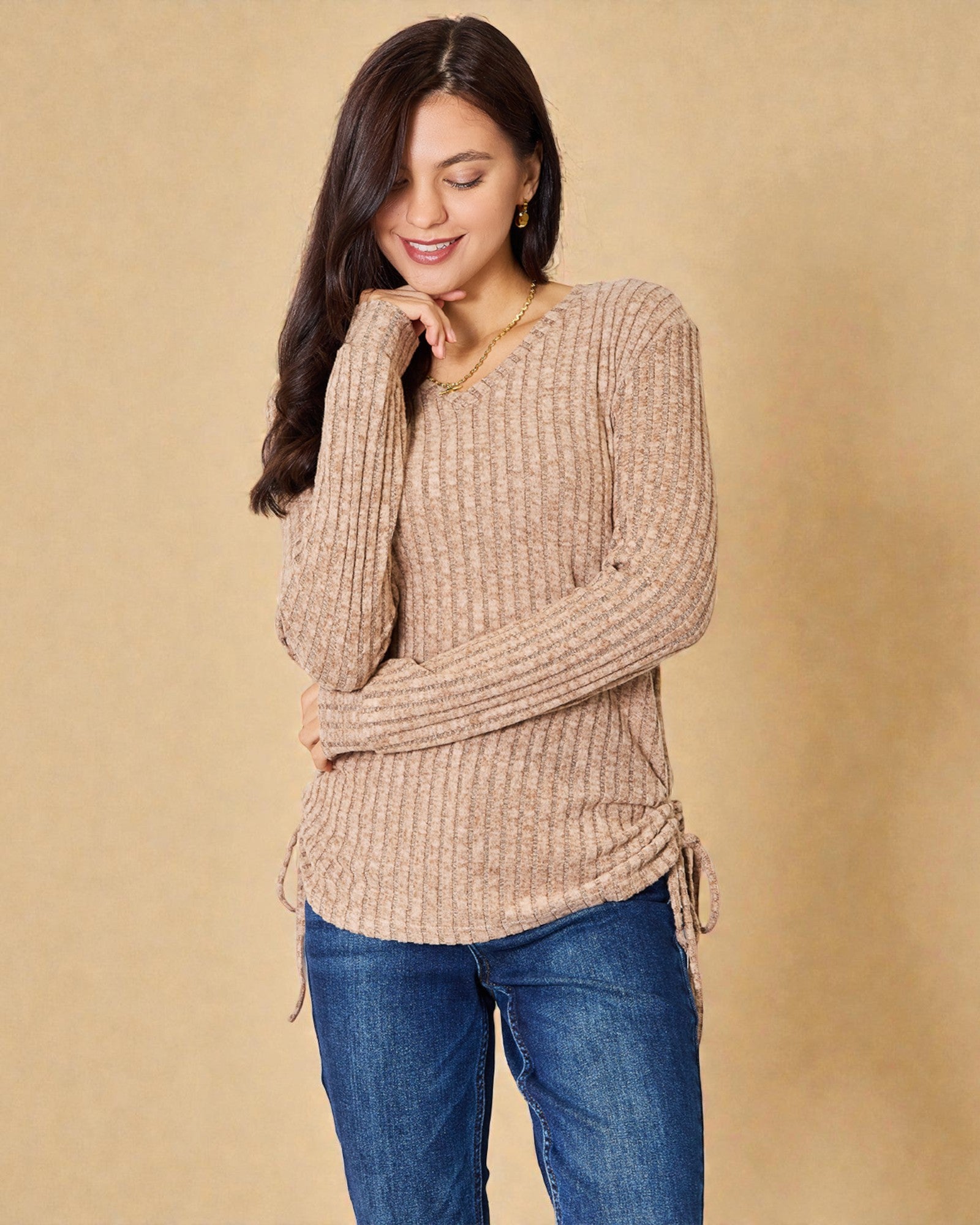 Woman wearing a beige sweater and blue jeans against a beige background